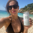 A 3x3 collage of nine lifestyle photos showing different people outdoors and indoors holding and drinking from clear glass bottles labeled BS by Nature's Path.